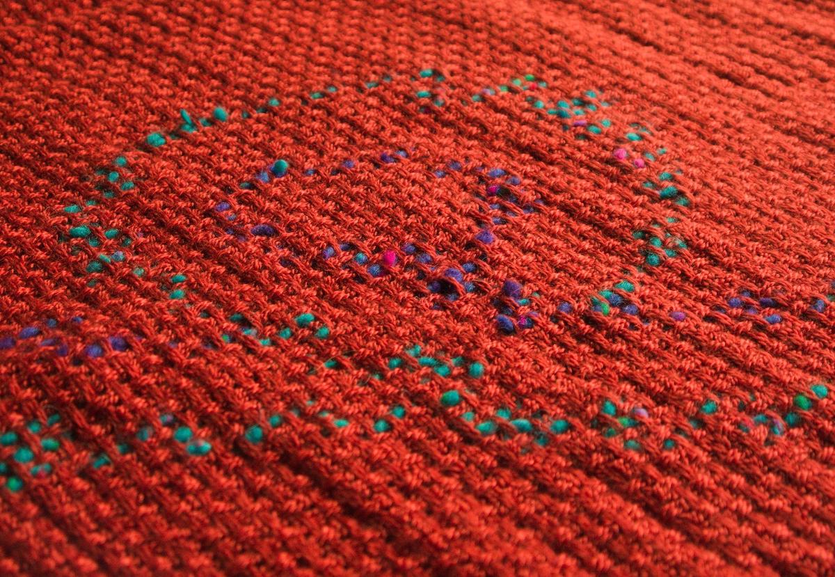 a low-angle view of the shawl, showing the inlaid wool bound between the red grid lines.
